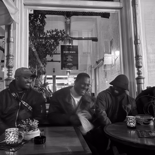 Pious, en bob, avec des amis à une table de café le soir, des bougies sur les tables.