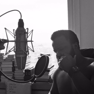 En noir et blanc : Pious est assis près d'un micro de studio, le menton dans la main, à côté d'une fenêtre lumineuse.