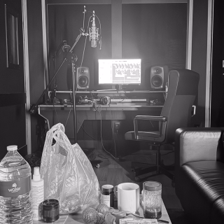 Un studio d'enregistrement : un micro et des enceintes sur le bureau, des boissons et des snacks sur la table devant.